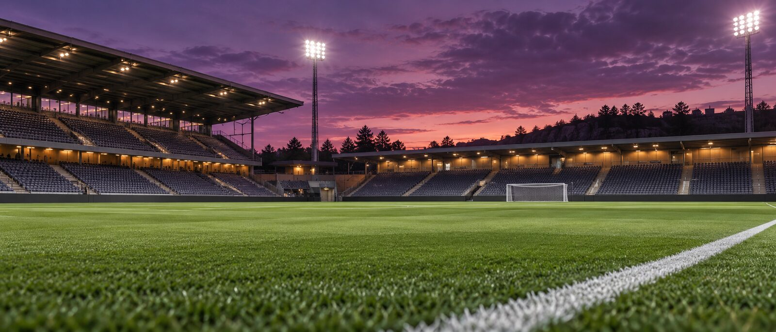 Fotbollsarena i skymning med plommonfärgad himmel och tänd belysning